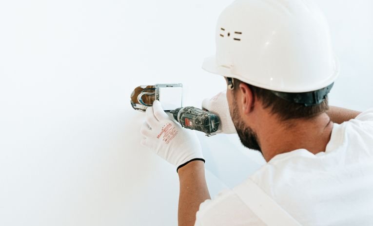 Man using a power tool to fix a white wall